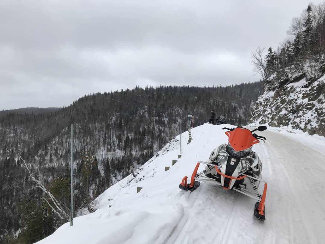 A snowmobile stoped on a trail beside a cliff hundreds of feet above a valley