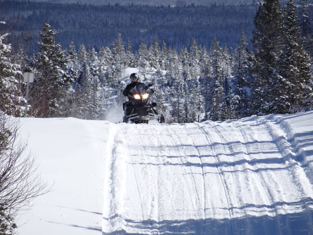 A snowmobiler cresting a hill riding towards the camera