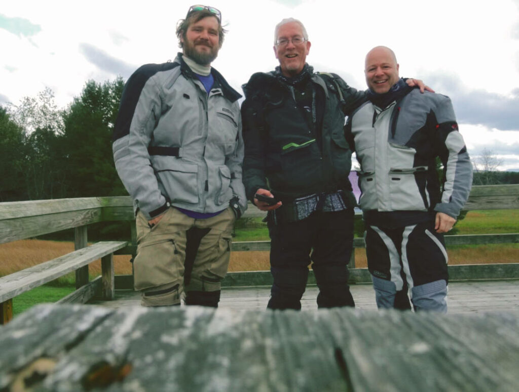 a photo of three men in motorcycle gear smiling for the camera