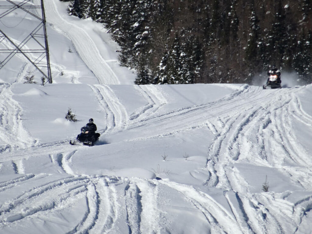 a photo of 2 snowmobiles on the trail on a mountainside