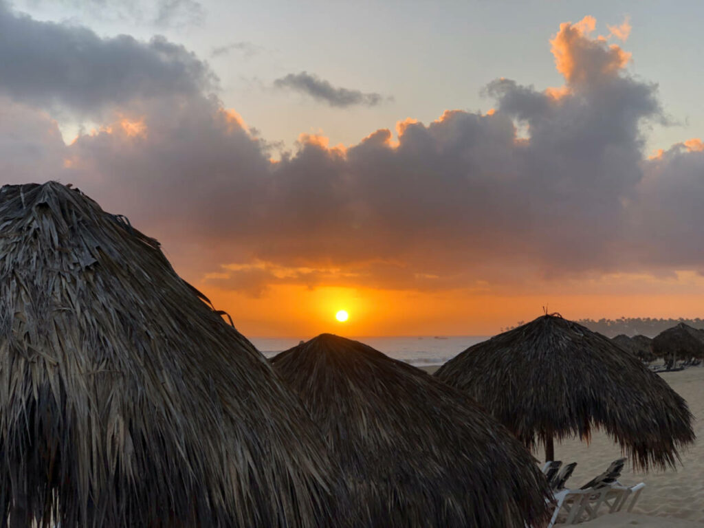 a photo of the sunrise over some grass huts in the caribbean